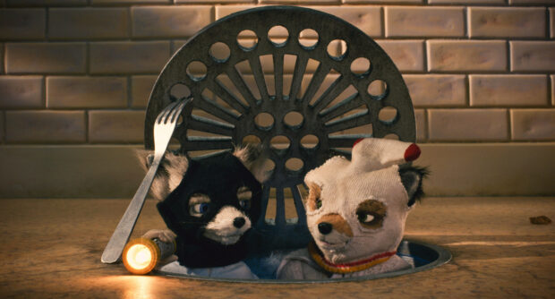 Two Fantastic Mr Fox characters wearing masks inside a metal drain on the kitchen floor holding a flashlight and a fork