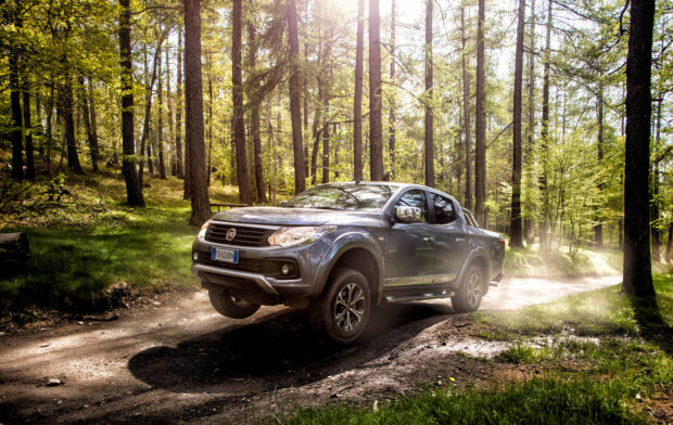 A Fiat Fullback driving on a sunlit forest trail with dust rising behind the truck, 2K Desktop Wallpaper