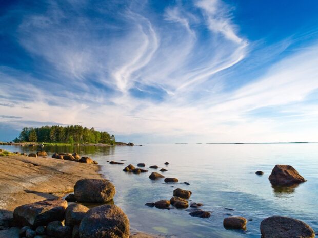 Rocky coastline and distant forest in Finland under a blue sky with wispy clouds