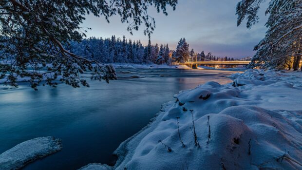 Snow covered riverbank and bridge in a Finland winter landscape at dusk