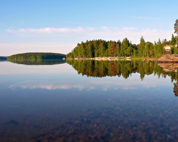 Calm Finland lake with green forest reflecting on water surface at sunrise