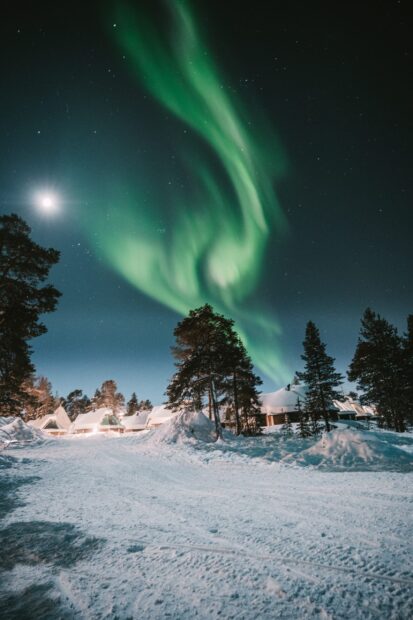 Snowy landscape with green aurora lighting up the Finland sky at night