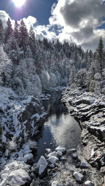 A serene river flowing through a snowy forest in Finland with clear skies and sun shining