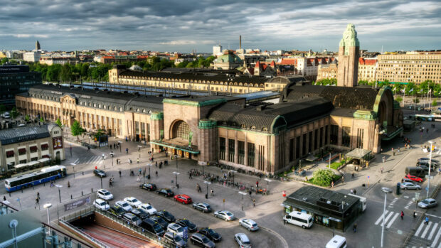 Historic Helsinki train station in Finland with cityscape and vehicles in daylight clouds