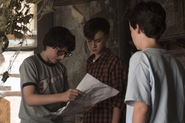 Finn Wolfhard and friends closely examine a mysterious paper in a dim room, HD Desktop Wallpaper