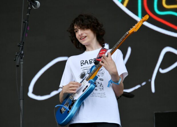Finn Wolfhard is performing on stage playing a blue electric guitar and smiling, 2K Desktop Wallpaper