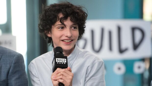 Finn Wolfhard wallpapers showing him holding a microphone and smiling during an interview, HD Desktop Wallpaper