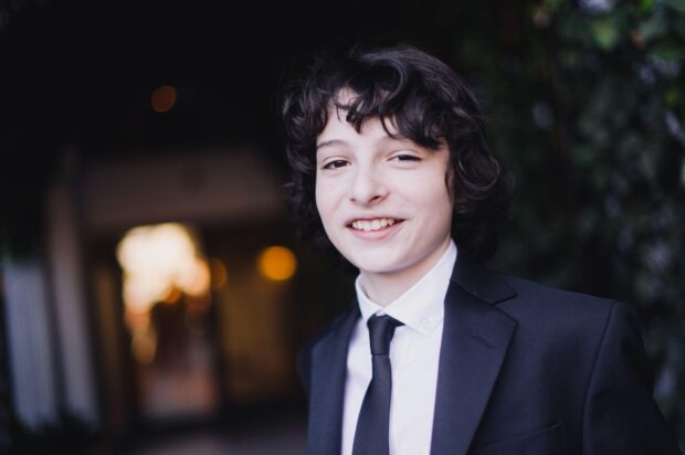 A young Finn Wolfhard is wearing a black suit and tie while smiling warmly, HD Desktop Wallpaper