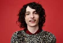 Finn Wolfhard is smiling wearing a patterned sweater against a red background, HD Desktop Wallpaper