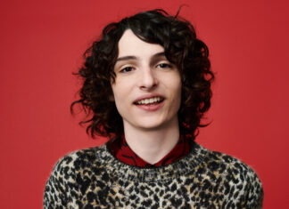 Finn Wolfhard is smiling wearing a patterned sweater against a red background, HD Desktop Wallpaper