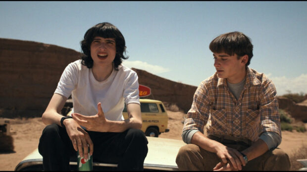 Finn Wolfhard and a friend sit casually in a desert setting with a van in the background, HD Desktop Wallpaper