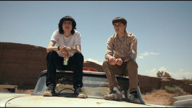 Finn Wolfhard with a friend sitting on the hood of a car in a desert setting, HD Desktop Wallpaper