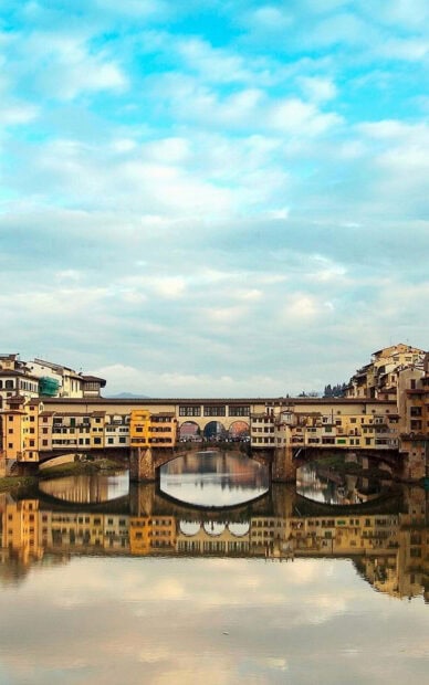 The Florence Wallpapers show the Ponte Vecchio bridge reflected in the calm river under a cloudy sky, HD Phone Wallpaper