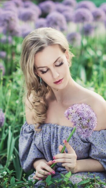 Woman holding purple flower in a flower field with lush green plants and soft natural light