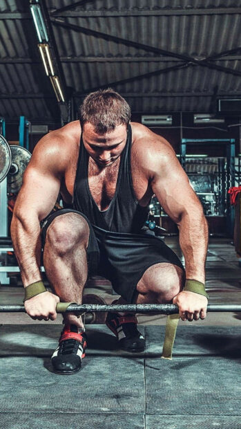 A muscular man grips the bar preparing for a powerlifting lift in the gym, 2K Phone Wallpaper