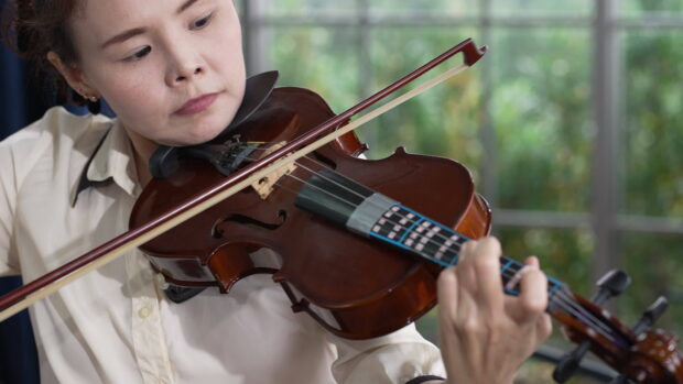 A woman is focused on playing violin strings indoors with natural light coming through the window, 4K Desktop Wallpaper