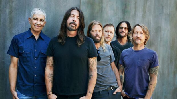 The Foo Fighters band members stand together in casual outfits against a plain background