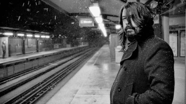 A man stands alone at a snowy subway platform in a reflective mood featuring Foo Fighters wallpaper
