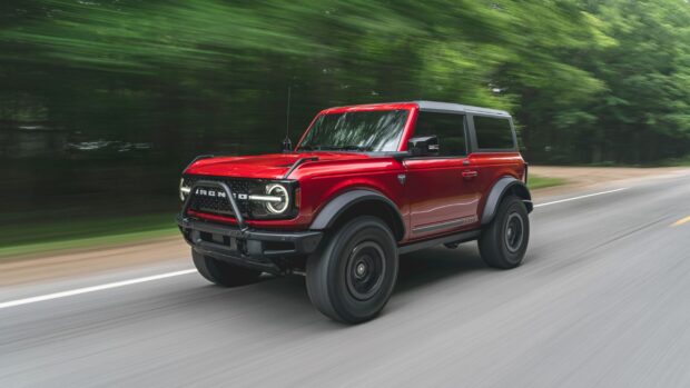 A red Ford Bronco driving fast on a forest road