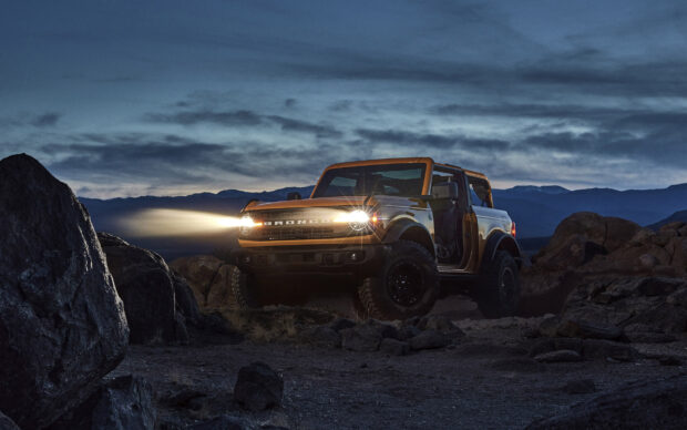 Ford Bronco driving off road with headlights on during twilight in rocky terrain