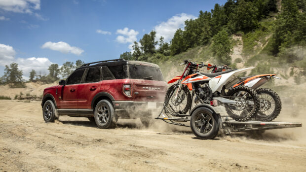 Red Ford Bronco towing motocross bikes on a dusty off road trail