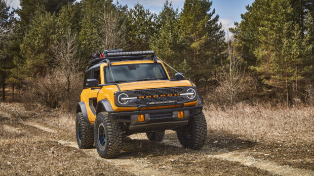Yellow Ford Bronco with off road tires driving on a dirt path surrounded by trees
