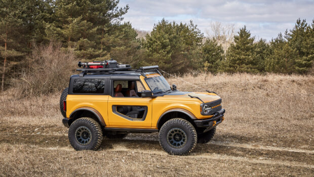 Yellow Ford Bronco with offroad tires parked on a grassy field near pine trees