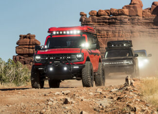 A red Ford Bronco driving on a rocky desert trail with other Broncos in the background