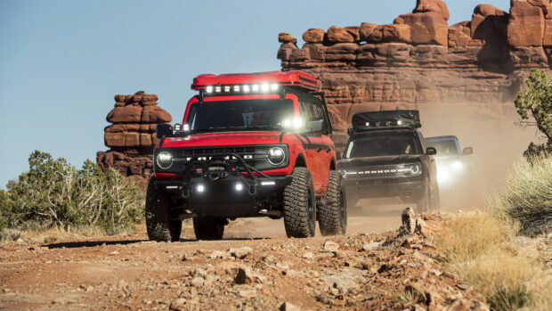 A red Ford Bronco driving on a rocky desert trail with other Broncos in the background