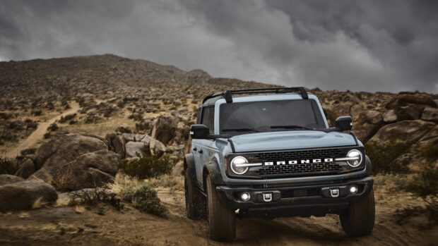 A rugged Ford Bronco driving through a rocky desert trail under cloudy skies