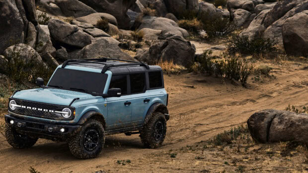 Blue Ford Bronco driving on a rocky dirt trail in a desert environment