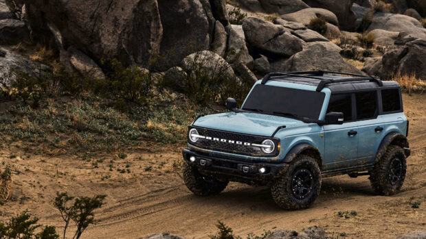 Blue Ford Bronco driving through a rocky desert terrain with mud on the tires