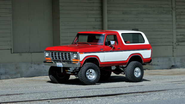 Classic Ford Bronco truck in red and white with large tires parked on gravel