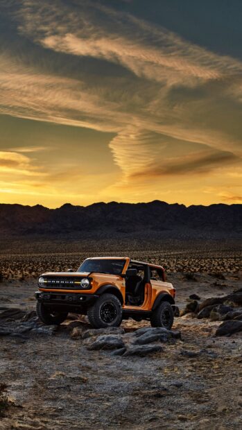 Orange Ford Bronco parked on rocky desert terrain under dramatic sunset sky