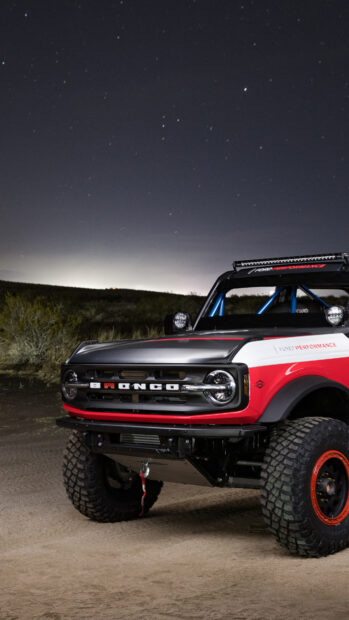 Red and white Ford Bronco with offroad tires under starry night sky