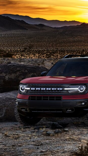Red Ford Bronco parked in rocky desert landscape during sunset with mountains in the background