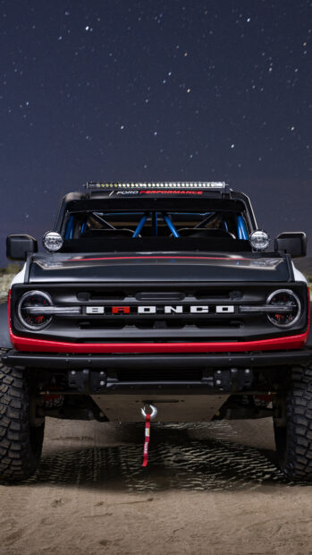 A front view of a custom Ford Bronco with off road tires and a starry night sky background