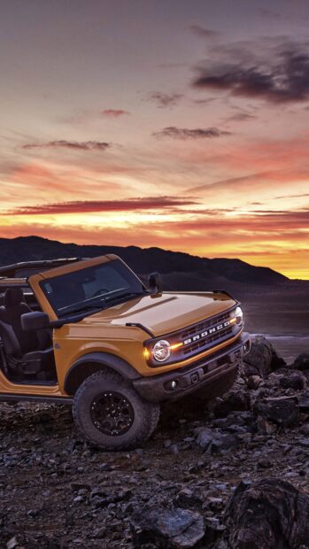 Yellow Ford Bronco climbing rocky terrain at sunset in a desert landscape