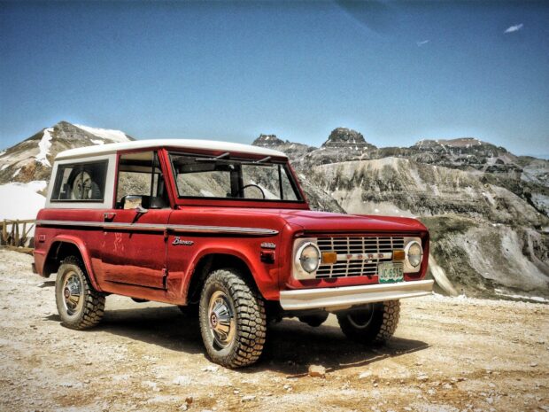 A classic Ford Bronco parked on mountain terrain under a clear blue sky