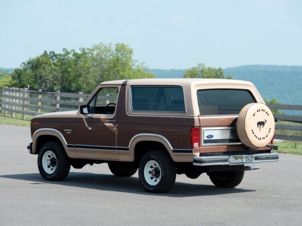 A classic Ford Bronco parked on a road with trees and hills in the background