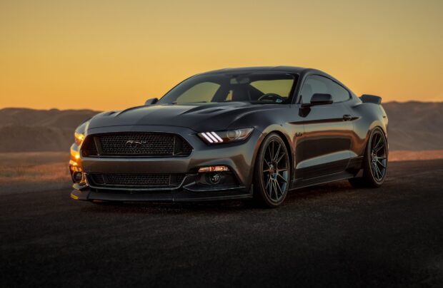 A sleek Ford Mustang parked on a road during sunset with mountains in the background