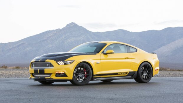 Yellow Shelby GT car on road with mountain background and clear sky