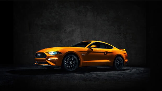 Orange Ford Mustang parked in a dark room with highlighted headlights and sporty design