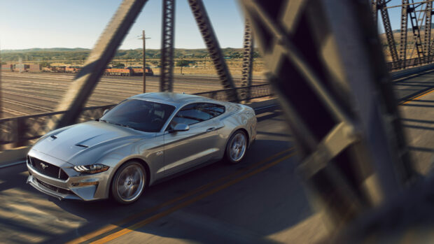 Silver Ford Mustang driving on a bridge with a desert landscape in the background