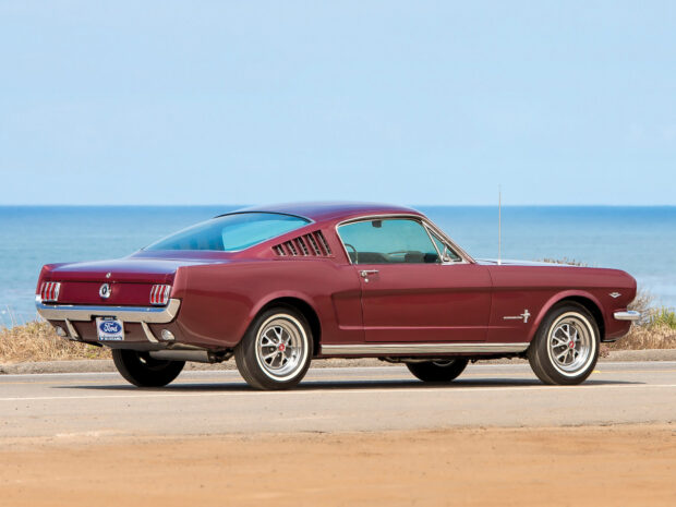 Classic Ford Mustang car parked near the ocean with a clear blue sky in the background