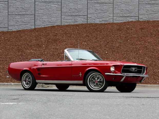 Classic red Ford Mustang convertible parked on the street with a stone wall backdrop