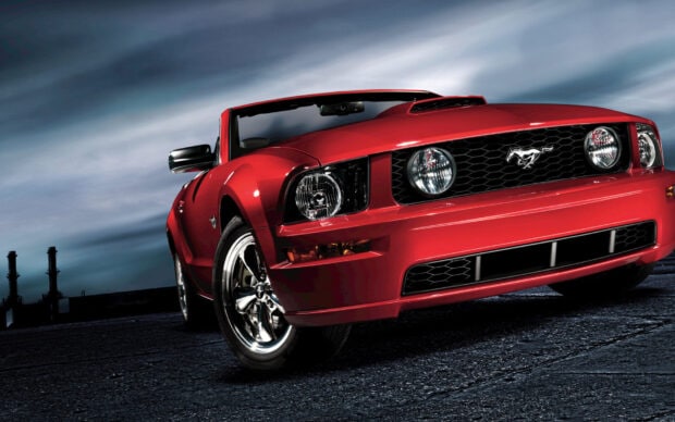 Red Ford Mustang car front view on a road under a cloudy sky