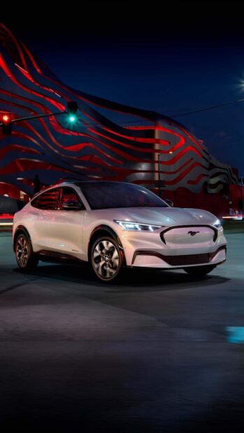 White Ford Mustang parked on city street with modern building at night