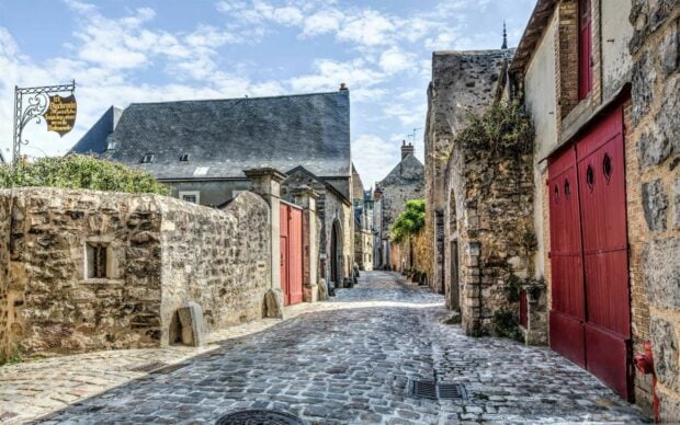 A charming France street with old stone walls and red doors under a blue sky