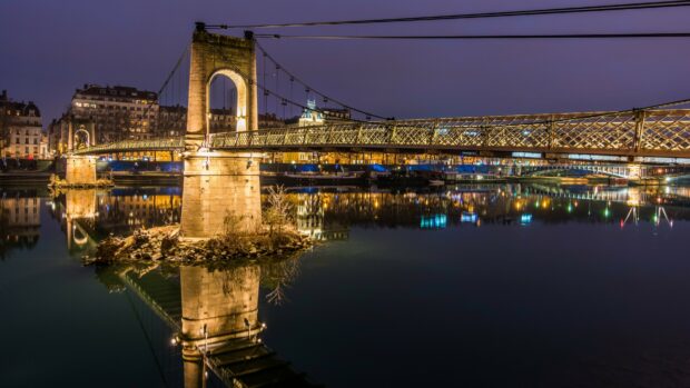 Night view of the France suspension bridge with city lights reflecting in calm water